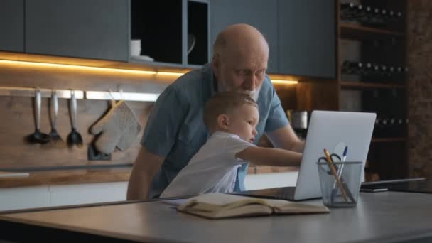 Großvater und Enkel sitzen zu Hause zusammen am Laptop, lernen Laptop, kommunizieren miteinander, zeigen auf Laptop-Bildschirm. Großvater bringt seinem Enkel die Arbeit am Laptop bei. — Stockvideo