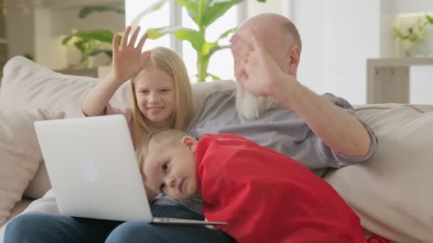 İletişim ailesi, iki torun ve yaşlı büyükbaba video konferansında webcam üzerinden görüntülü sohbet ediyorlar, çocuklar uzaktan anne ve babalarıyla el sallıyorlar.. — Stok video