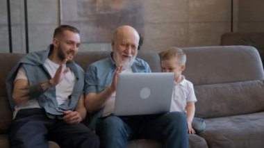 Mutlu aile, yaşlı dedesi ve tatlı çocuğu olan bir baba dizüstü bilgisayar ekranına bakıyor akrabalarıyla görüntülü sohbet yoluyla selamlaşan eller sallıyor..