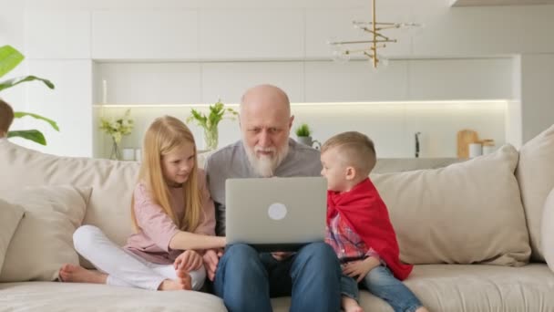 Família feliz de gerações, avô de cabelos grisalhos idosos com netos, menino e menina, rir emocionalmente ao assistir vídeos engraçados e engraçados olhando para laptop enquanto sentado em casa no sofá. — Vídeo de Stock