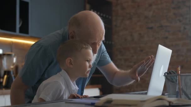 Großvater bringt Jungen bei, am Laptop zu arbeiten. Freundschaft zwischen Großvater und Enkel, zu Hause neben Laptop sitzen und miteinander kommunizieren, mit den Händen gestikulieren. — Stockvideo