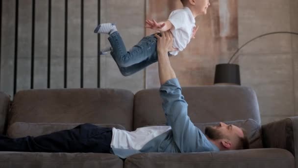 Feliz relación familiar entre padre e hijo. Lindo chico rubio juega juego con su padre en avión, vuela en brazos de su padre, niño vuela como avión extiende sus brazos a un lado. — Vídeos de Stock