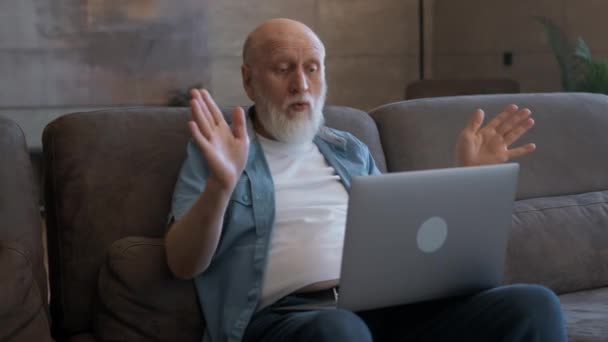 年长的老人通过视频链接、微笑和手势与家人交谈，情感地展示他的双手，看着笔记本电脑屏幕，坐在家里。通过视频聊天与儿童沟通. — 图库视频影像