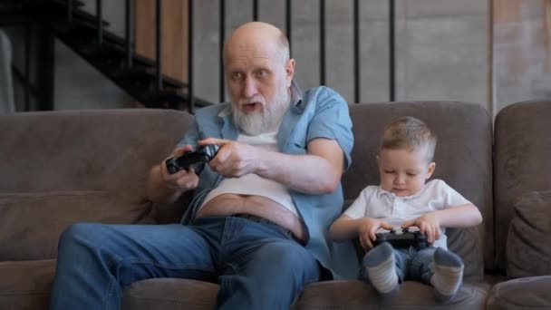 Happy family grandfather plays video game with his boy grandson at home. Mature man and boy use game joysticks. Older man wins in computer game. Happy grandfather celebrate victory. — Stock Video