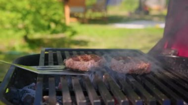 Şef ızgarada ızgara ve demir spatulayla hamburgerler için sulu et hazırlıyor. Hazır hamburger yemek için ateşte et pişirmek. Izgara ızgaralı lezzetli burger. Izgarada ızgara.