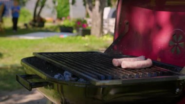 Aşçı mangal panelinde sosis hazırlıyor. Kömürün üstünde et hazırlıyor. Festivalde taze ızgara yemek. Erkek eli, taze taze çiğ, organik domuz sosisini ızgaranın üzerine koyar..