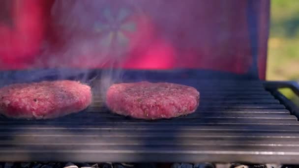ジューシーな2つのカツビーフバーガーは、灰と炎の火花とバーベキューグリルで強火で揚げられています。路上でハンバーガーピクニックを調理.バーベキューグリルでおいしいバーガー。バーベキューグリルでの料理 — ストック動画