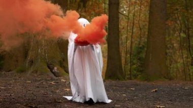 Cadılar Bayramı, Azizler Günü. Parti için hayalet kostümü. Cadılar Bayramı partisi için beyaz karnaval hayalet kostümü giymiş çocuk ormanda duruyor ve elinde şeytani Jack Balkabağı 'nı tutuyor..