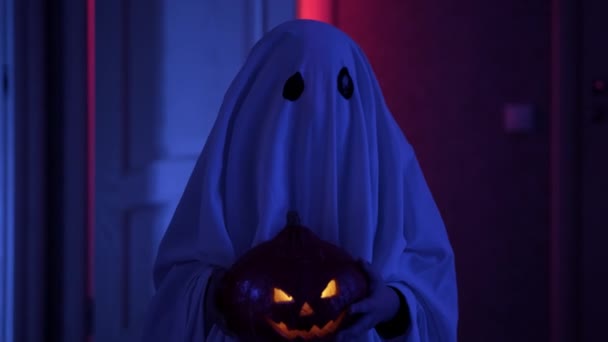 Portrait of creepy ghost standing in scary corridor in moonlight with thunderstorm and holding glowing pumpkin Jack with creepy face in his hands. Child in carnival ghost costume for Halloween. — Stock Video