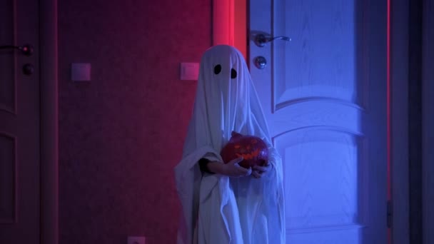 All Hallows Eve, All Saints  Eve. Boy in ghost costume at Halloween. Portrait of scary ghost holding glowing pumpkin jack walking along dark corridor in moonlight at night and peppery thunderstorm. — Stock Video