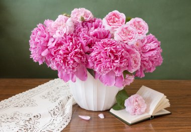 Tahta bir masanın üzerinde açık bir kitap olan bir buket şakayık.