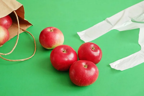 many red apples on paper bag vs polyethylene bag on green background, green grocery concept, zero waste