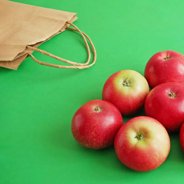 many red apples and paper bag on green background, green grocery concept, zero waste concept