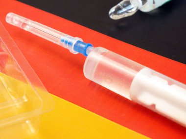 Aşılı şırınga, Almanya bayrağının arka planında, Coronavirus aşısına karşı eldiven olarak kullanılıyor.