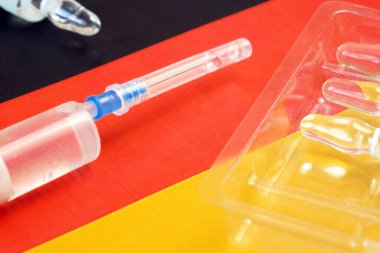 Aşılı şırınga, Almanya bayrağının arka planında, Coronavirus aşısına karşı eldiven olarak kullanılıyor.