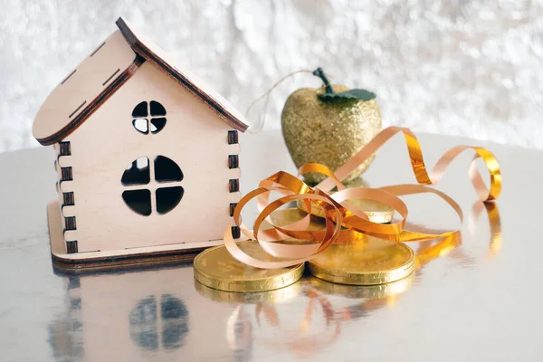 wooden house model, gold chocolate coins and new year decorations on shining background with copy space, xmas background, Welth concept. New year sales for new houses, closeup