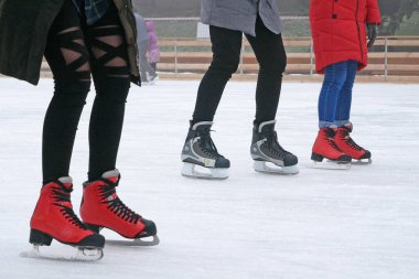 Buz pateni ayakkabısı giyen insanlar buz pateni pistinde açık havada kayıyorlar.