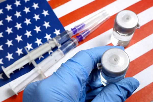 bottle a vaccine is held by hand in a glove on background of the USA flag, vaccine against coronavirus, closeup