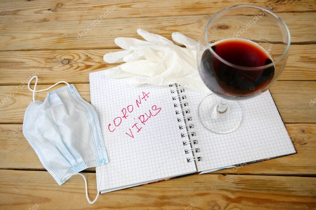 word coronavirus in notebook, medical gloves, medical mask and glass of wine, closeup