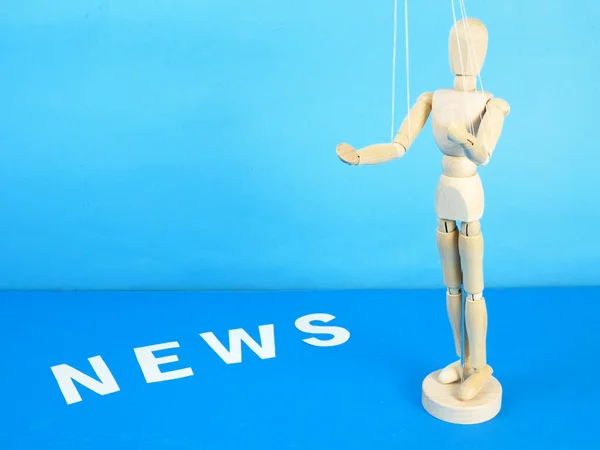 control a marionette by strings on fingers and word news on blue background, closeup