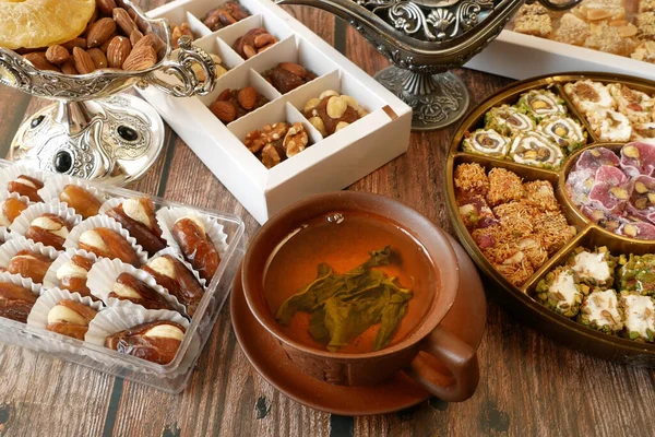 Eastern sweets with nuts, candy, metal vase, tea, dates on wooden background, closeup