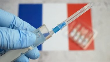 Aşılı şırınga, Fransız bayrağının arka planında, Coronavirus aşısına karşı bir eldivenin içinde elle tutulur.
