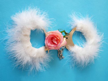 Mavi arka planda gül çiçekleri olan beyaz tüylü kelepçeler, nazik seks oyunları konsepti