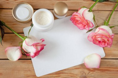 Şişede krem kozmetik, taze pembe gül çiçekleri ve taç yaprakları, doğal kozmetik konsepti.