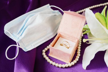 Hediye kutusu, mavi tıbbi maske, altın alyans, inci kolye ve pembe çiçek demeti, düğün ve koronavirüs konsepti, yakın plan.