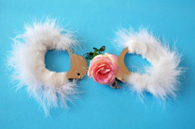 Mavi arka planda gül çiçekleri olan beyaz tüylü kelepçeler, nazik seks oyunları konsepti, yakın plan.