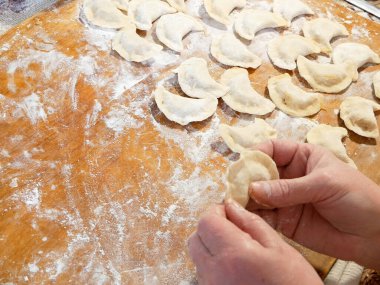 Ev yapımı mantı, ravioli veya sebzeli pelmeni yapma süreci. Tahtada raviyolis pişirmeye hazır, bir kadın elini tutuyor, yakın plan.