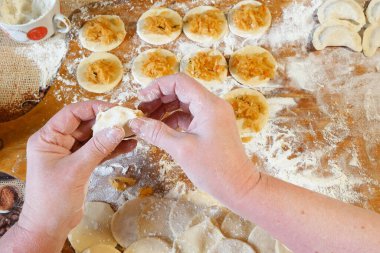 Ev yapımı mantı, ravioli veya sebzeli pelmeni yapma süreci. Tahtada raviyolis pişirmeye hazır, bir kadın elini tutuyor, yakın plan.