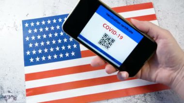 Cep telefonundaki aşı pasaportunun görüntüleri el altında seyahat olanağı sağlıyor ve arka planda Amerikan bayrağı. Coronavirus Covid 19 'a karşı aşı. Dokunulmazlık veya Sağlık pasaportu, yakın plan