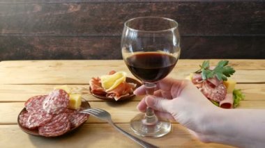Bardakta kırmızı şarap ve soğuk tütsülenmiş et tabağı. Antipasto, ahşap tabakta. Şarap ve soğuk tütsülenmiş et tabağı dilimlenmiş jambon, jambon ve pastırma..  