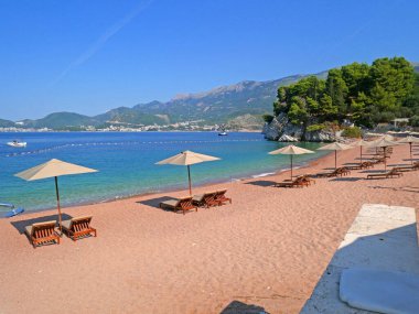 Karadağ 'ın Sveti Stefan kenti yakınlarında şezlong sandalyeli ve şemsiyeli lüks kumsal. Açık havada.