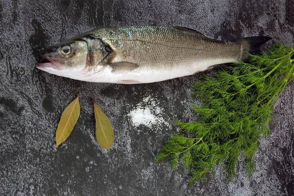 fresh sea bass fish cooking with greens on black background, top view, closeup