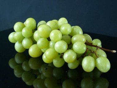 Siyah arkaplanlı yeşil üzüm. Bir grup yeşil üzüm seriliyor, yakın plan