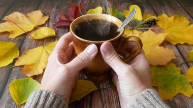 Sonbahar yaprakları masada, bir fincan sıcak kahve ve kadın elleri sıcak kazak içinde, sonbahar havası konsepti. 