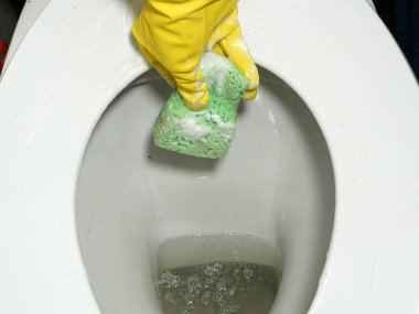 Sarı lastik eldivenli eller tuvaleti temizliyor. Tuvaleti tuvalet fırçasıyla temizlemek. Yakın çekim.