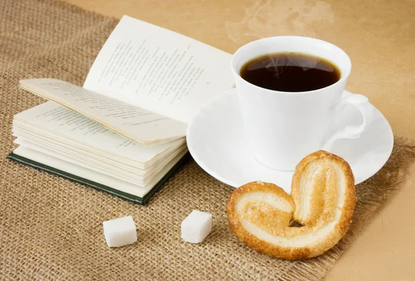 Cup of hot coffee with sugar, cake, spoon and book — Stock Photo, Image