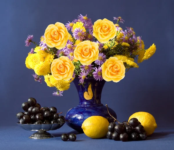 Huge bunch of autumn flowers and yellow roses, lemon and grapes on dark blue background — Stock Photo, Image