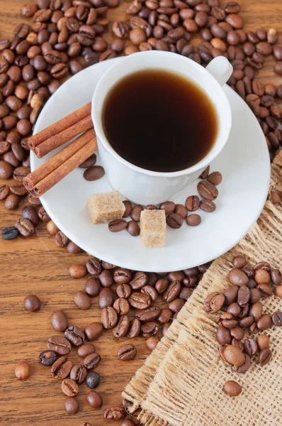 Φλιτζάνι καφέ, μπαχαρικών και καφέ φασόλια σε ξύλινο τραπέζι και σάκο φόντο — Φωτογραφία Αρχείου