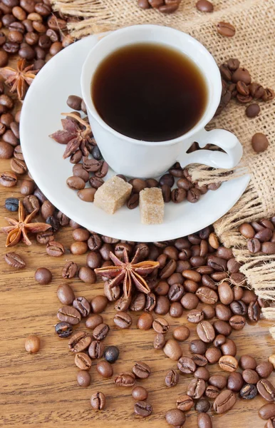 Cangkir kopi, rempah-rempah dan biji kopi di atas meja kayu dan latar belakang karung — Stok Foto