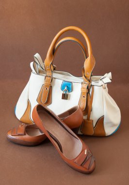 Kahverengi arka planda kadın çantası ve sandaletleri var.