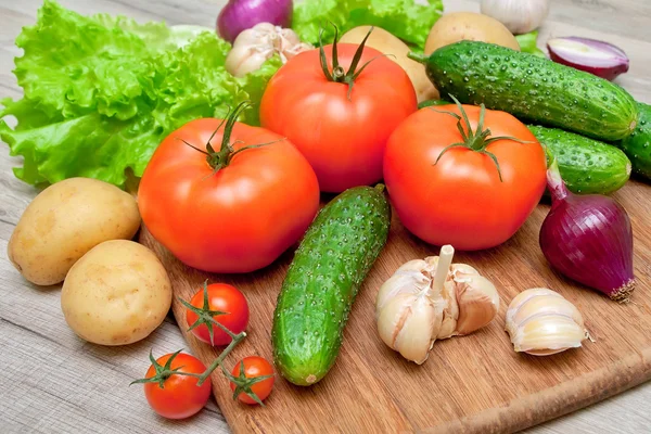 Tomates maduros e outros legumes em uma tábua de corte — Fotografia de Stock