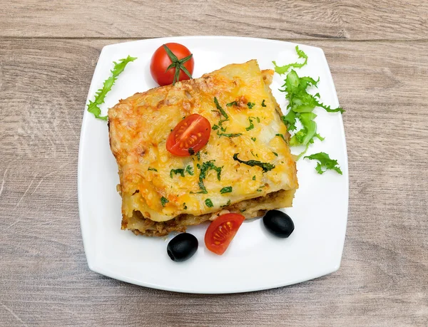 Lasagna with meat, tomatoes, olives and greens on a plate — Stock Photo, Image