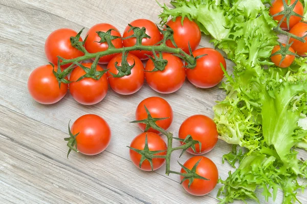 Tomates cereja e alface sobre um fundo de madeira — Fotografia de Stock