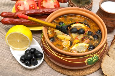 Dish of russian hodgepodge soup and other food on a wooden table clipart