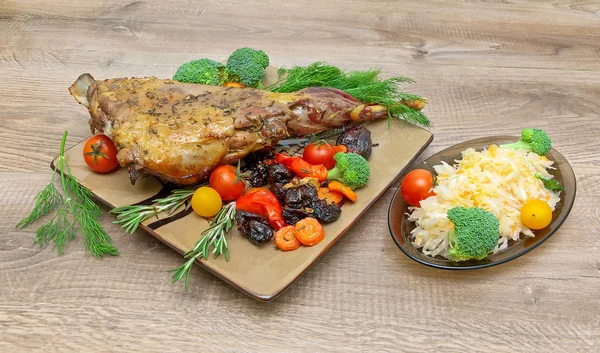 Roasted leg of lamb with vegetables and herbs on a wooden backgr — Stock Photo, Image