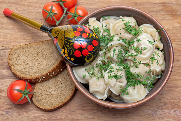 Русская кухня: пельмени на тарелке, помидоры черри и хлеб
